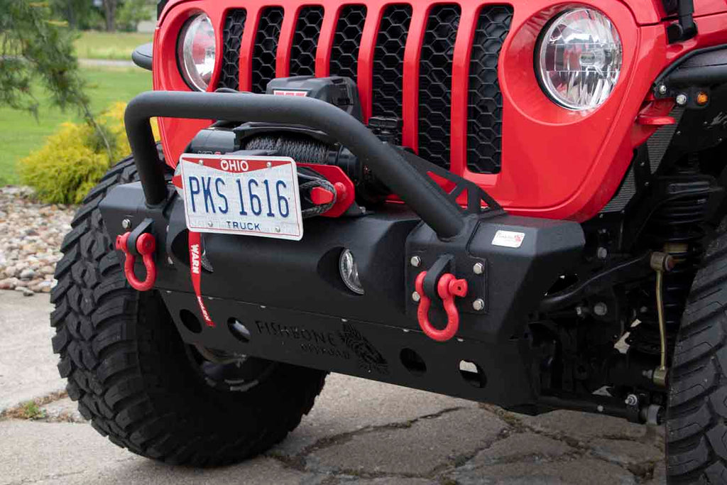 Fishbone Offroad Front Stubby Winch Bumper, perfectly contoured under a Jeep grill, showcasing durability and rugged elegance.