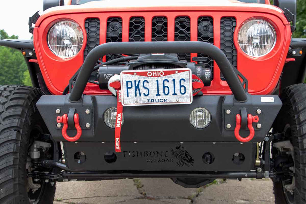 Fishbone Offroad Front Stubby Winch Bumper, perfectly contoured under a Jeep grill, showcasing durability and rugged elegance.