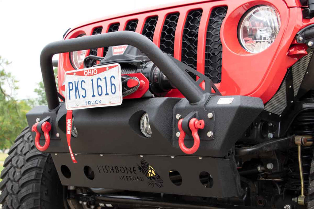 Fishbone Offroad Front Stubby Winch Bumper, perfectly contoured under a Jeep grill, showcasing durability and rugged elegance.